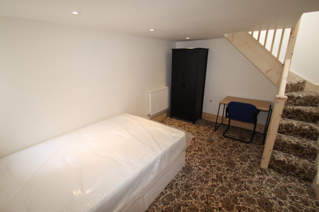 student bedroom with double bed, black two door wardrobe, desk and chair, stairs leading upstairs to property