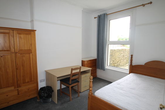 student bedroom with double bed, chest of drawers, large two door wardrobe with drawers underneath and desk with chair and drawers