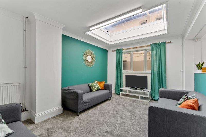 shared living room with three grey sofas, television on tv stand and turquoise feature wall 