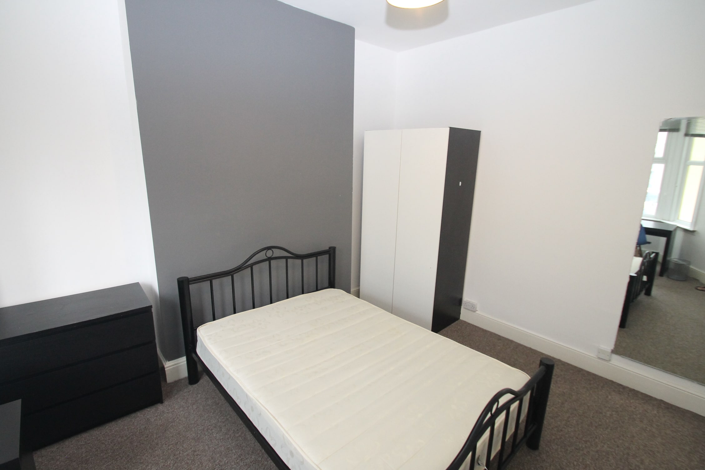 Second student bedroom with double bed, two door wardrobe, black chest of drawers, full length mirror and desk with chair in front of windows
